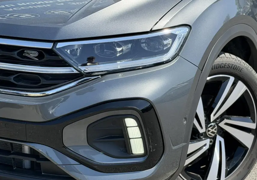 Gros plan sur l'avant droit du Volkswagen T-Roc gris Indium, mettant en valeur le projecteur Matrix LED et la jante Nevada 18 pouces.