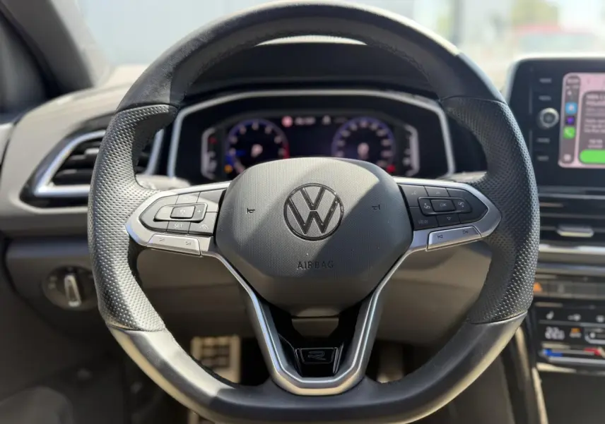 Vue rapprochée du volant sport en cuir noir avec logo R-Line du Volkswagen T-Roc 2025, tableau de bord digital en arrière-plan.