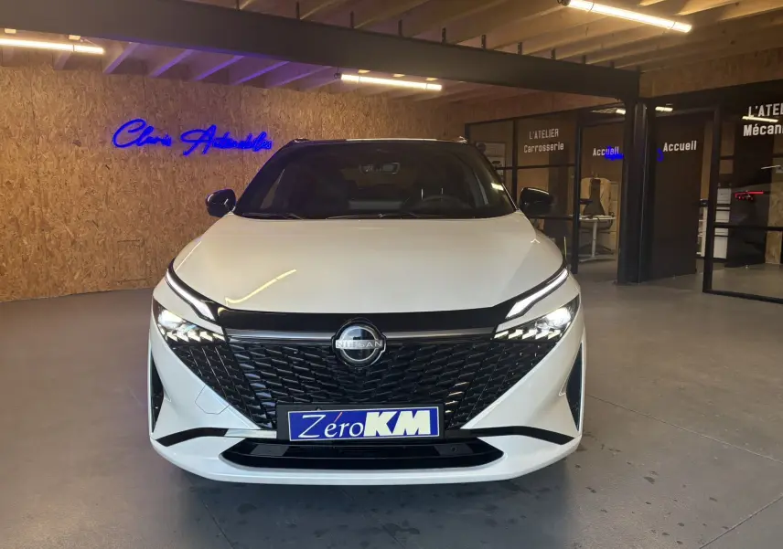 Vue frontale d'un Nissan Qashqai blanc nacré avec toit noir, éclairage LED et calandre noire brillante dans un showroom.
