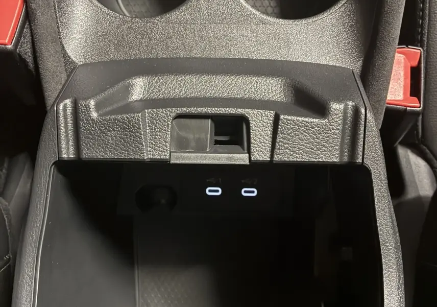 Gros plan sur la console centrale noire du Nissan Qashqai 2025, avec porte-gobelets et ports USB éclairés.