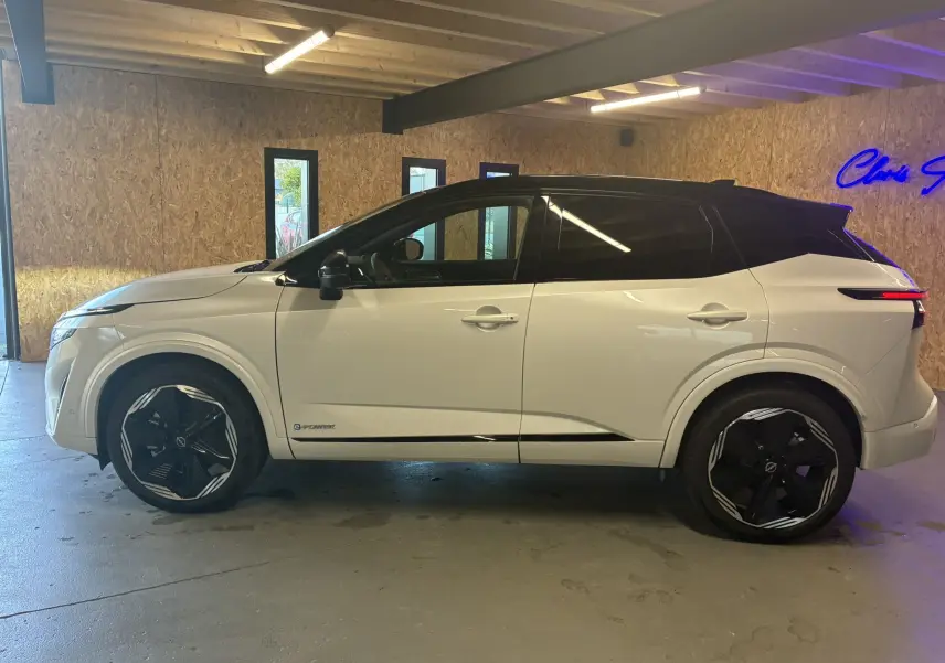 Vue latérale gauche du Nissan Qashqai 2025 blanc nacré avec toit noir et jantes noires au design moderne.