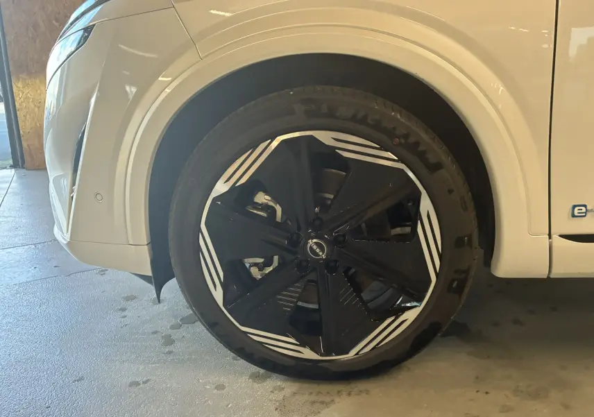 Gros plan sur la roue avant gauche du Nissan Qashqai blanc nacré avec jante noire et motifs blancs distinctifs.