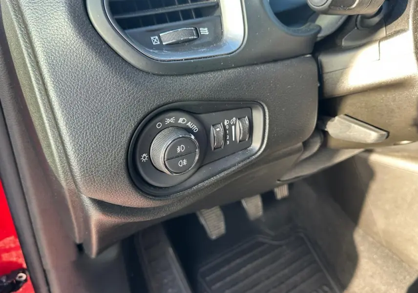 Gros plan sur le tableau de bord côté gauche du Jeep Renegade rouge, montrant la commande des phares et les pédales.