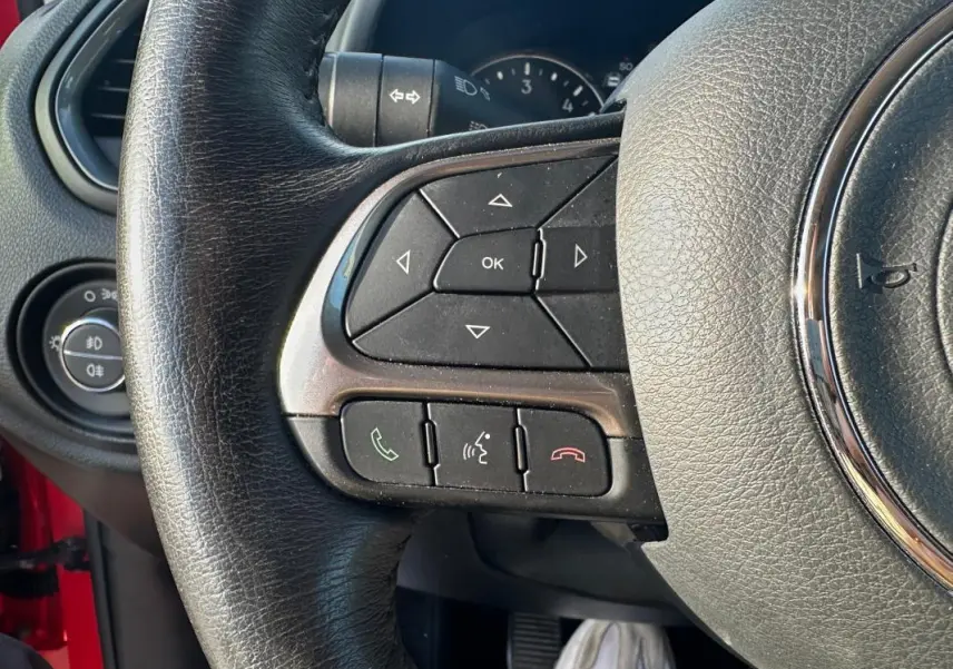 Gros plan sur le volant noir du Jeep Renegade rouge, montrant les commandes intégrées et le tableau de bord partiel.