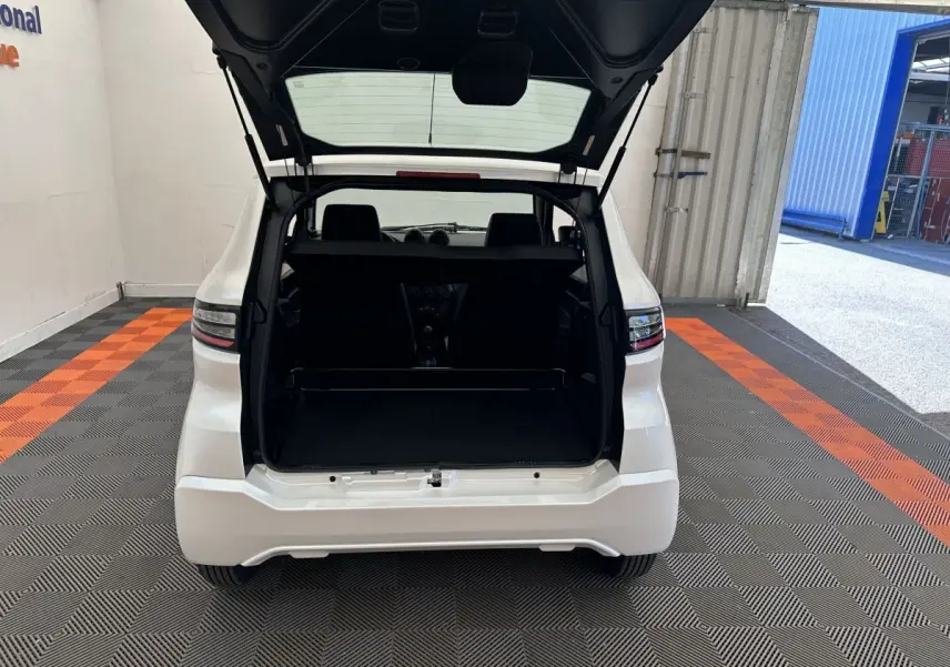 Vue arrière d'une AIXAM AMBITION E CITY PACK blanche 2025 avec coffre ouvert dans un garage éclairé.