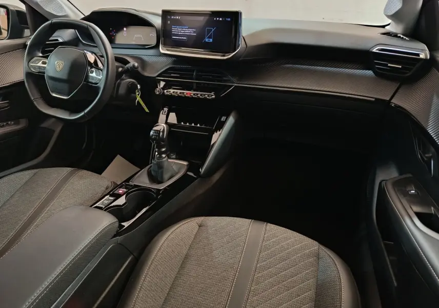 Intérieur de la Peugeot 208 PureTech 100 S&S Allure 2025, vue côté conducteur, tableau de bord gris foncé avec écran tactile.