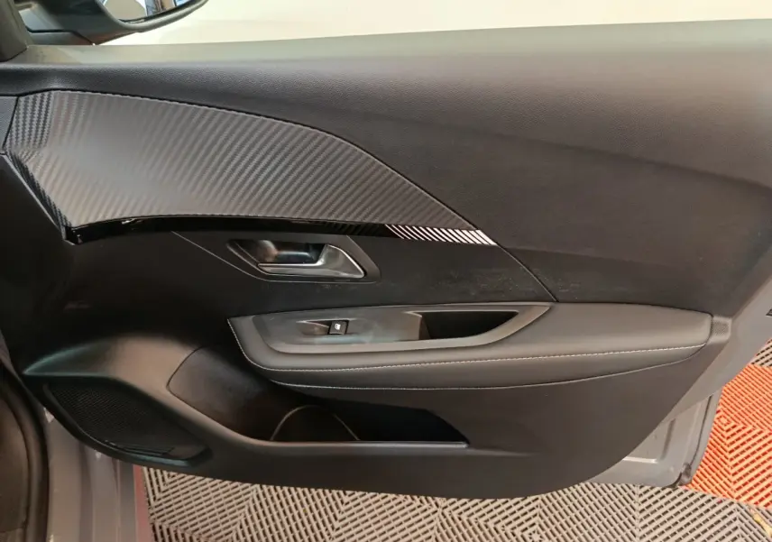 Vue intérieure côté gauche de la porte d'une Peugeot 208 gris foncé avec insert imitation carbone et commande de vitre.