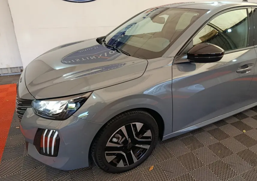Vue 3/4 avant droit d'une Peugeot 208 gris foncé avec phares allumés et jantes noires distinctives.