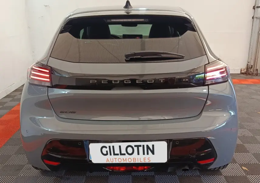 Vue arrière d'une Peugeot 208 gris foncé avec feux arrière allumés et logo Peugeot central sur le hayon.
