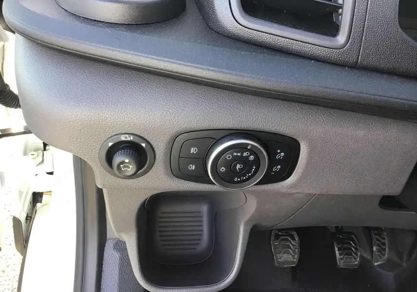 Gros plan sur le tableau de bord côté gauche du Ford Transit blanc, montrant les commandes d’éclairage et les pédales.