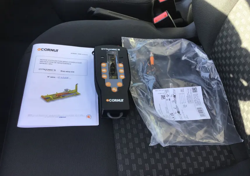 Vue intérieure sur siège avant droit montrant notice, télécommande et câble du bras de levage Cornut dans un Ford Transit blanc.