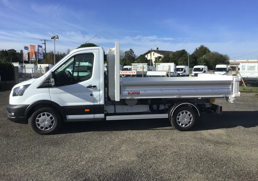 Vue de profil côté gauche d’un Ford Transit blanc avec benne polybenne et bras de levage, stationné en extérieur.