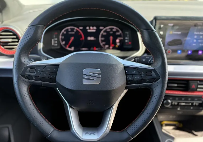 Vue rapprochée du volant perforé noir avec surpiqûres rouges et tableau de bord digital de la SEAT Ibiza TSI 115 FR 2025.