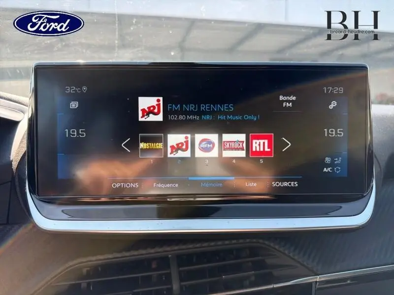 Écran tactile central du tableau de bord montrant la radio FM NRJ dans un Peugeot 2008 blanc nacré, vue de face.