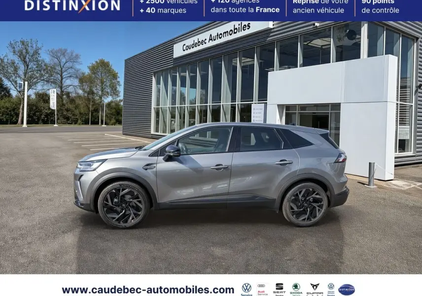 Profil droit de la Renault Symbioz E-Tech 160 ch gris métallisé, avec jantes alliage noires, devant un showroom.