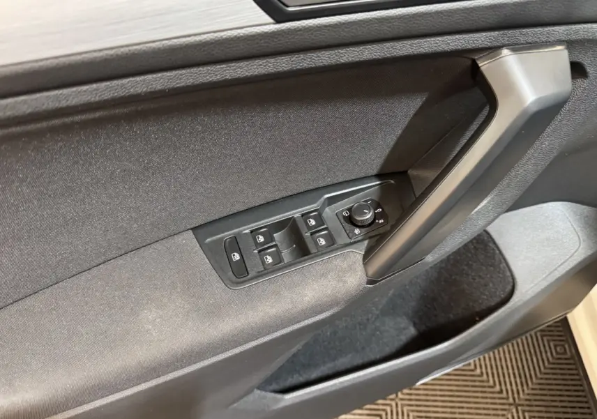 Gros plan sur la porte avant gauche du Volkswagen Tiguan blanc, montrant les commandes électriques des vitres et des rétroviseurs.