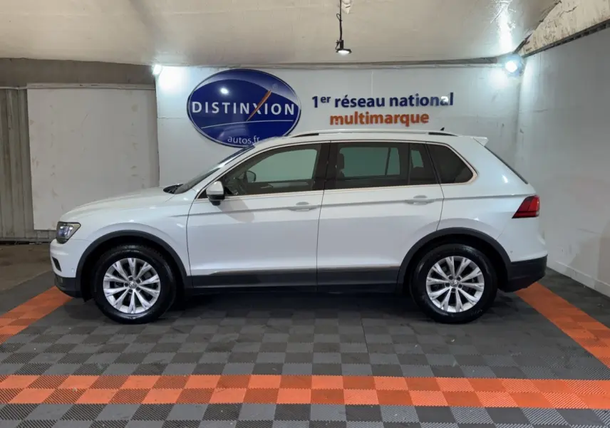 Profil côté gauche d'un Volkswagen Tiguan blanc 2020 stationné en intérieur avec jantes alliage et barres de toit noires.