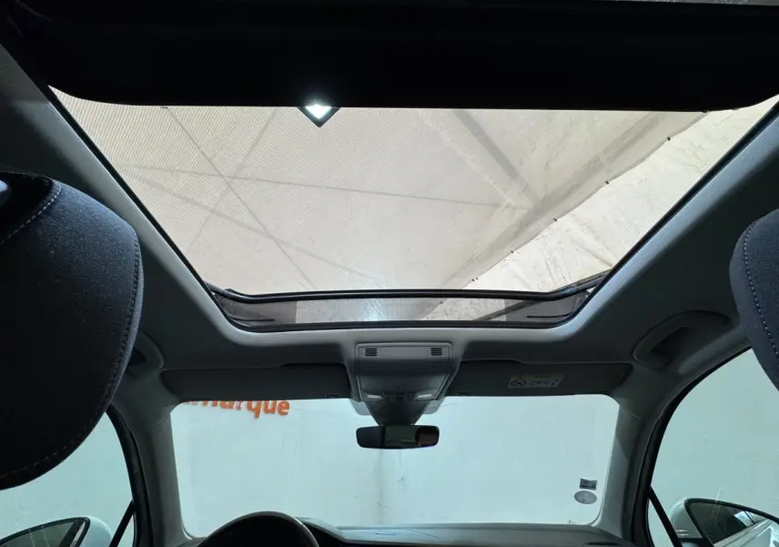 Vue intérieure du toit ouvrant panoramique du Volkswagen Tiguan blanc, avec tableau de bord et rétroviseur central visibles.
