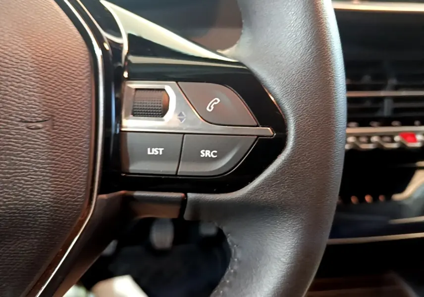 Gros plan sur le volant cuir multifonctions de la Peugeot 208 jaune, avec commandes audio et téléphone intégrées.