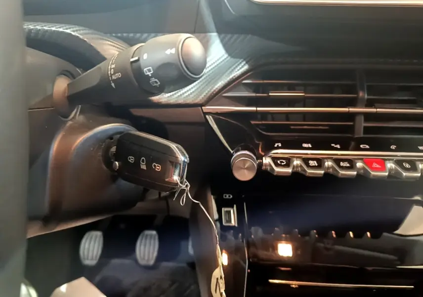 Gros plan sur le tableau de bord noir et la clé insérée dans le contacteur d'une Peugeot 208, côté conducteur.