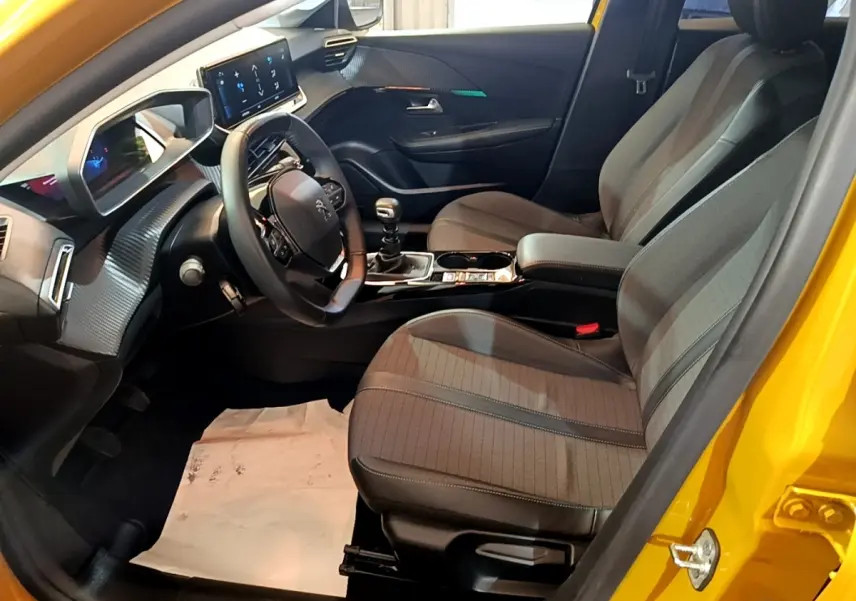 Intérieur avant droit d’une Peugeot 208 jaune 2023, volant cuir multifonctions et tableau de bord digital.