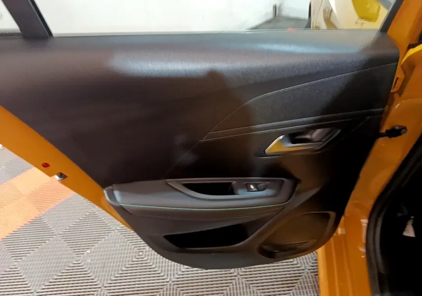 Vue intérieure de la porte arrière droite noire sur Peugeot 208 jaune, avec poignée et commande de vitre visible.