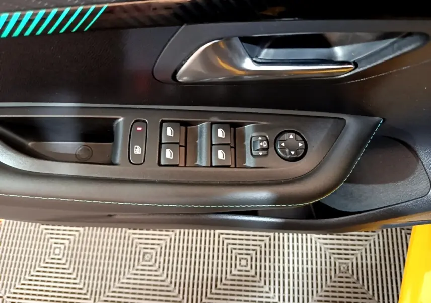 Gros plan sur la porte côté conducteur de la Peugeot 208 jaune, montrant les commandes électriques des vitres et rétroviseurs.