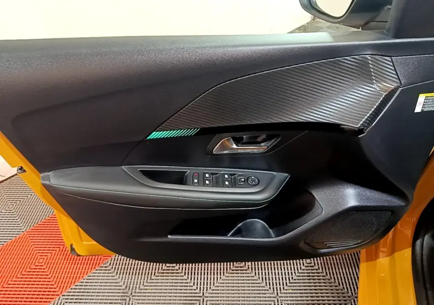 Vue intérieure de la porte avant gauche jaune de la Peugeot 208 2023 avec commandes électriques et insert décor carbone.
