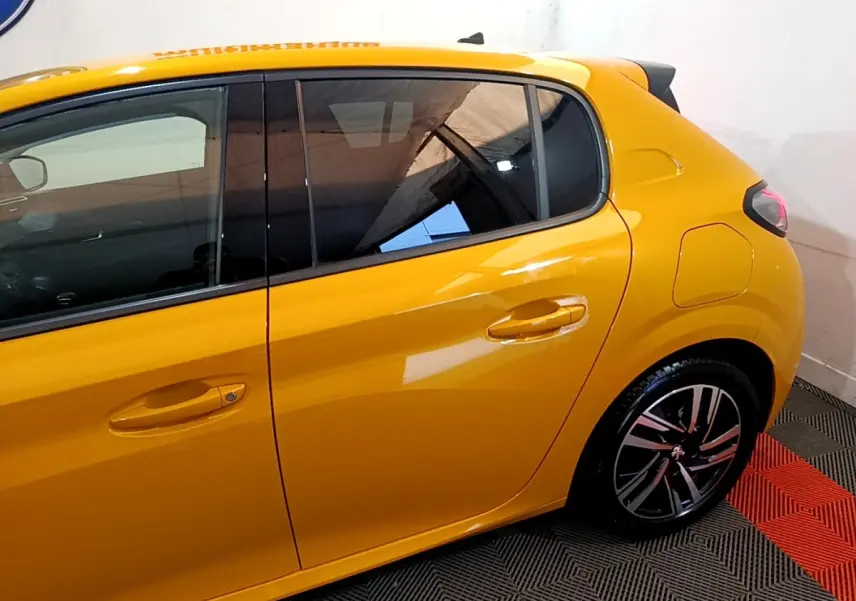 Vue côté droit arrière d'une Peugeot 208 jaune vif avec jante alliage et vitres teintées dans un intérieur showroom.