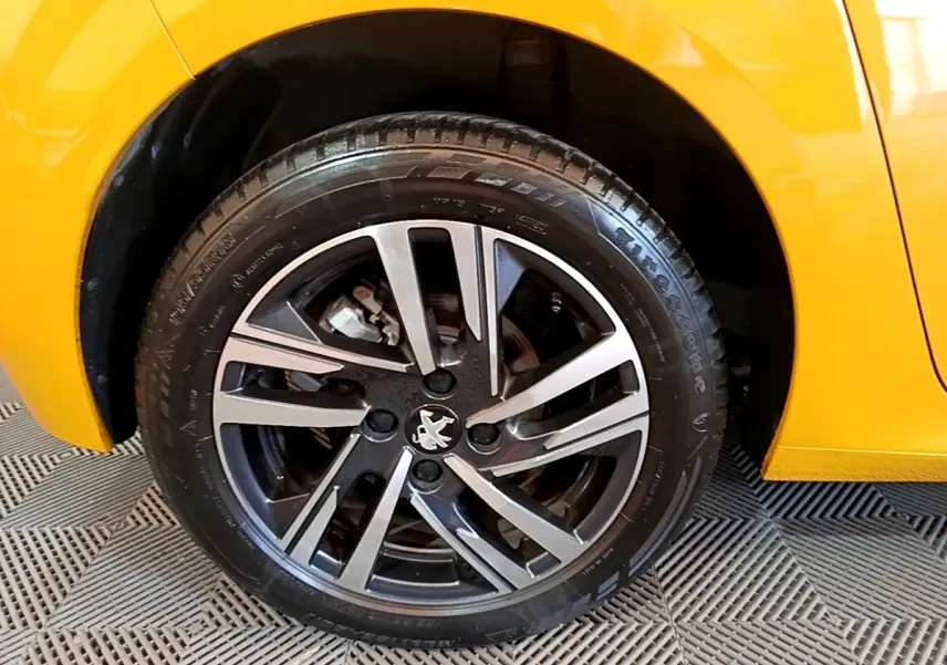 Gros plan sur la roue avant droite de la Peugeot 208 jaune, avec jante alliage noire et argentée au design moderne.