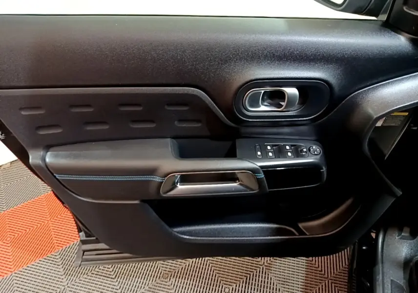 Vue intérieure côté gauche de la porte noire du Citroën C5 Aircross hybride avec commandes électriques et poignée chromée.