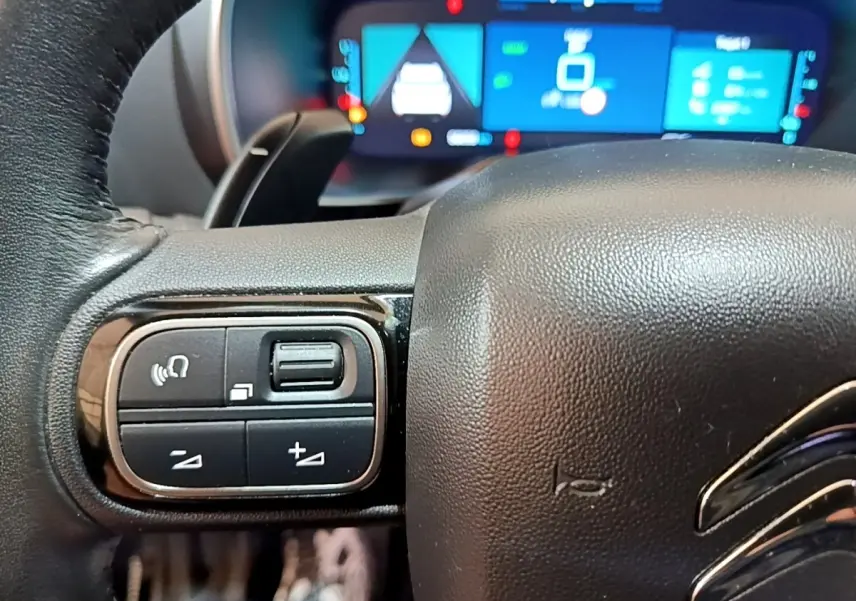 Gros plan sur le volant noir de la Citroën C5 Aircross hybride avec commandes intégrées et tableau de bord numérique en arrière-plan.
