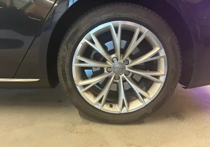 Gros plan sur la roue avant droite d'une Audi A8 noire 2016, jante alliage à design multiple branches.