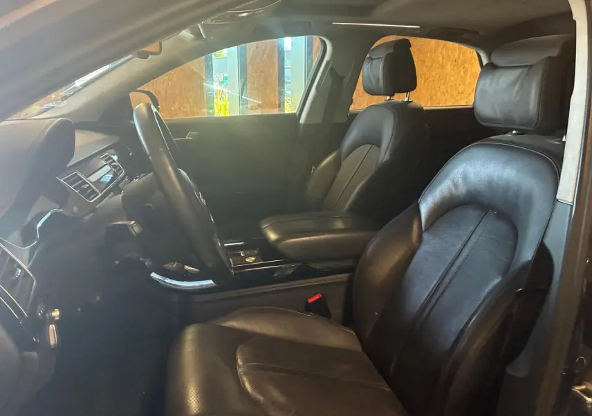 Vue intérieure côté gauche de l’Audi A8 2016 noire, montrant les sièges en cuir et le tableau de bord élégant.
