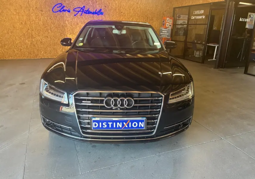 Vue avant d'une Audi A8 noire 2016 avec calandre chromée et plaques Distinxion dans un showroom.