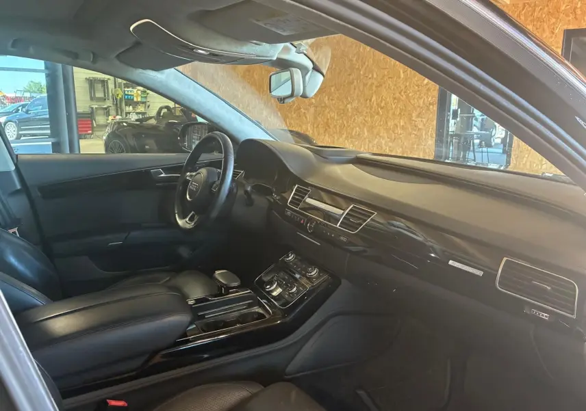 Intérieur noir de l'Audi A8 2016 vu côté conducteur, mettant en valeur le tableau de bord et la console centrale.