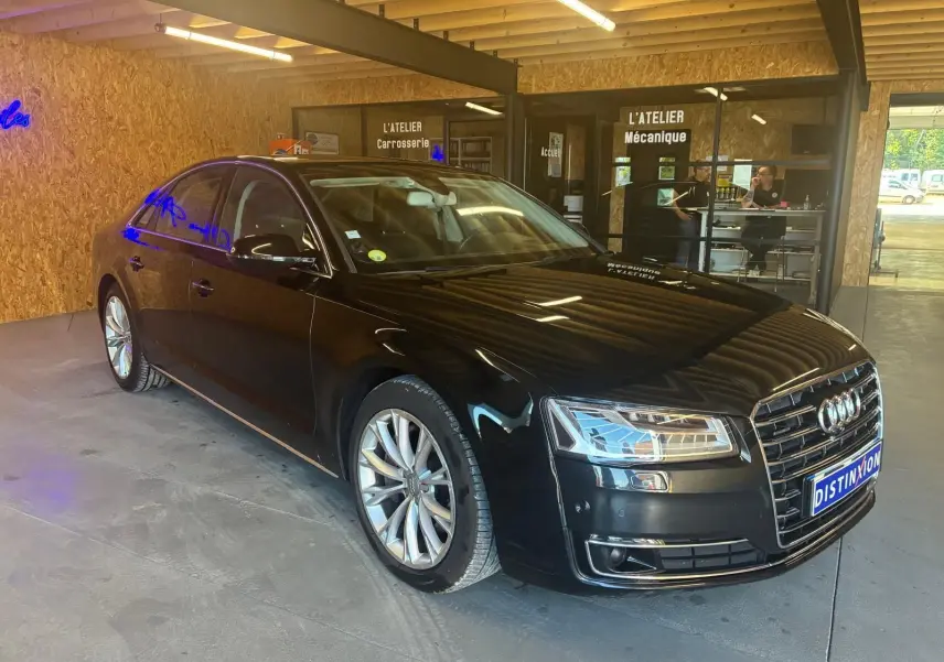 Audi A8 3.0 TDI noire vue en 3/4 avant droit dans un atelier avec reflets lumineux sur la carrosserie.