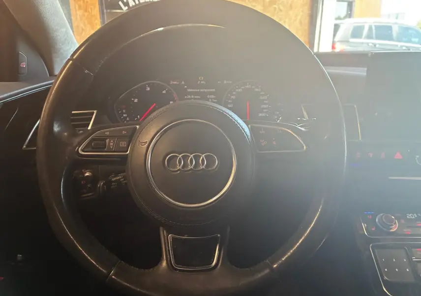 Vue rapprochée du volant noir de l'Audi A8 2016 avec commandes intégrées et tableau de bord numérique.