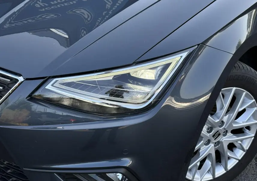 Gros plan sur l'avant droit gris magnétique d'une SEAT Ibiza TSI 115 Xcellence, mettant en valeur le phare et la jante alliage.