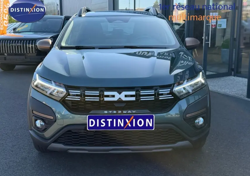 Vue de face d'une Dacia Sandero Stepway 2025 vert cèdre métallisé avec calandre noire et feux LED allumés.