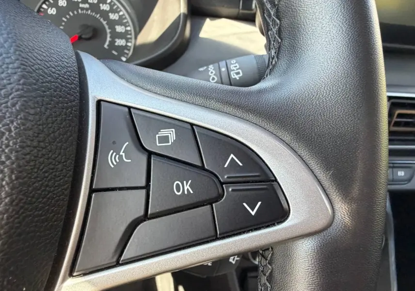 Gros plan sur les commandes multifonctions noires et argent du volant de la Dacia Sandero 2025, intérieur noir.