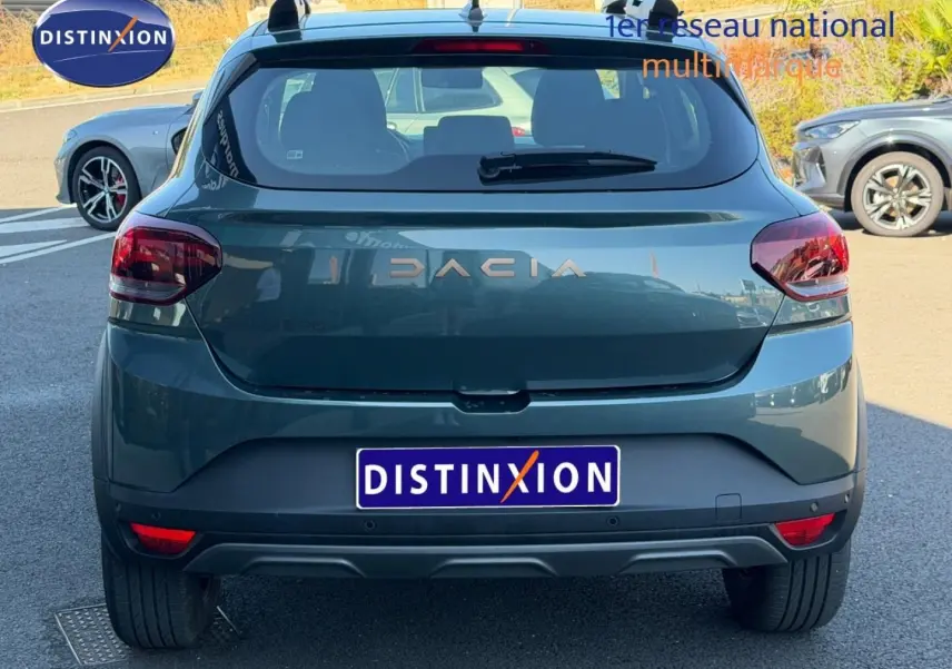 Vue arrière d'une Dacia Sandero 2025 vert cèdre métallisé avec barres de toit et feux arrière rouges.