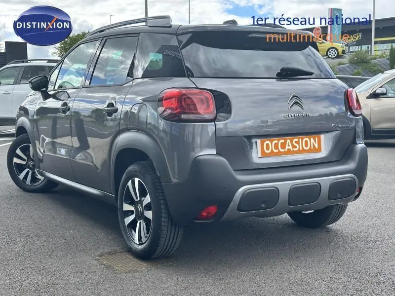Vue 3/4 arrière d'un Citroën C3 Aircross gris métallisé avec barres de toit et jantes alliage noires et argent.