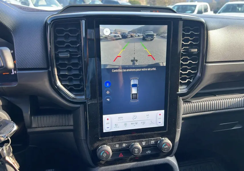 Vue intérieure du tableau de bord du Ford Ranger 2025 blanc glacier, avec écran tactile affichant la caméra de recul et commandes climatisation.