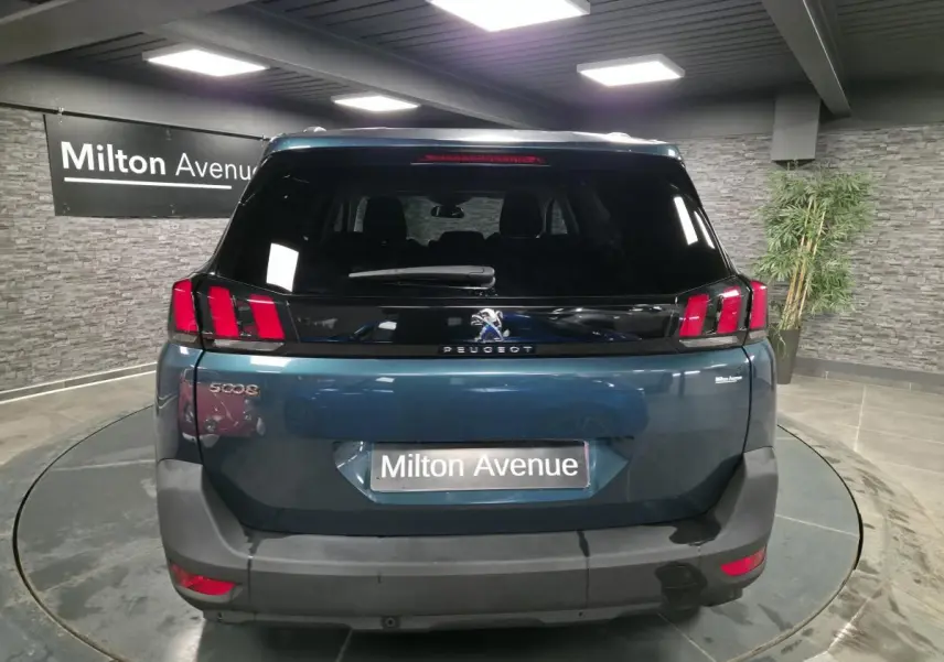 Vue arrière d'un Peugeot 5008 bleu métallisé avec feux arrière à griffes rouges dans un showroom.
