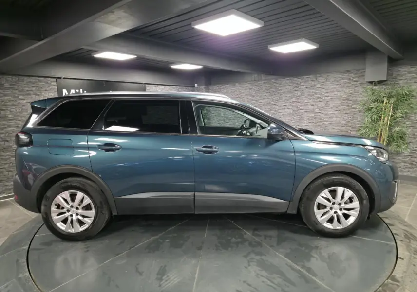 Profil droit d'un Peugeot 5008 bleu métallisé avec jantes alliage 17 pouces dans un showroom intérieur.