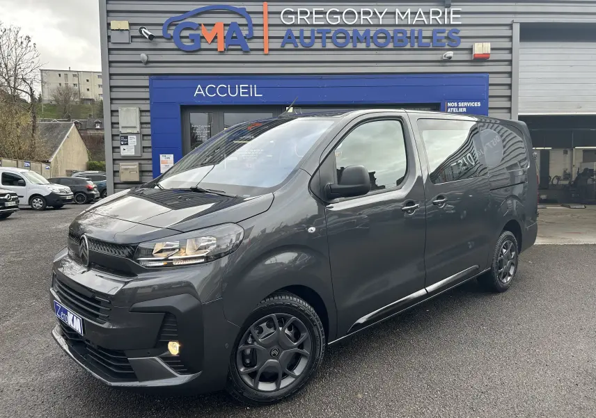 Vue 3/4 avant droit d’un Citroën Jumpy Cabine Approfondie gris titane métallisé garé devant un garage automobile.