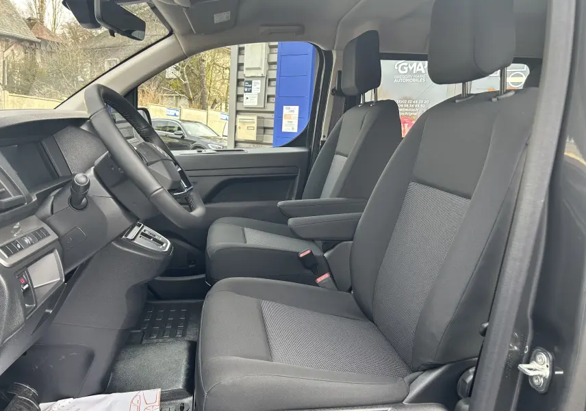 Vue intérieure côté conducteur du Citroën Jumpy cabine approfondie 2025, sièges tissu noir et console centrale visible.