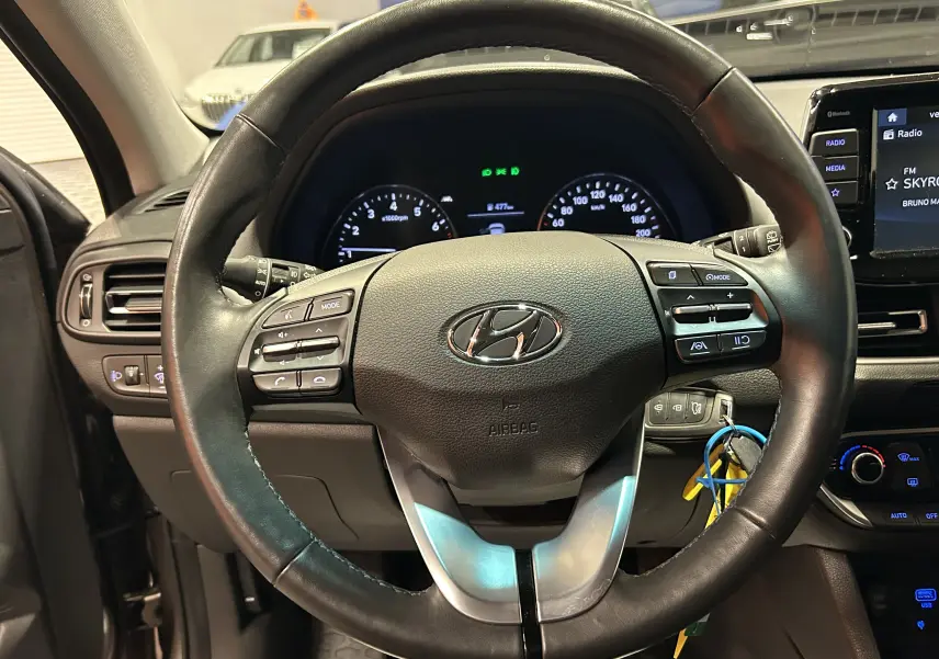 Vue rapprochée du volant cuir noir de la Hyundai i30 SW 2022 avec commandes intégrées et tableau de bord éclairé.