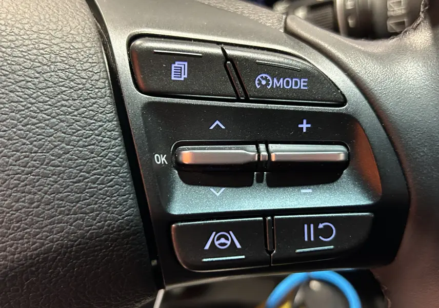Gros plan sur les commandes au volant à gauche du Hyundai i30 SW 2022, boutons noirs avec éclairage bleu.